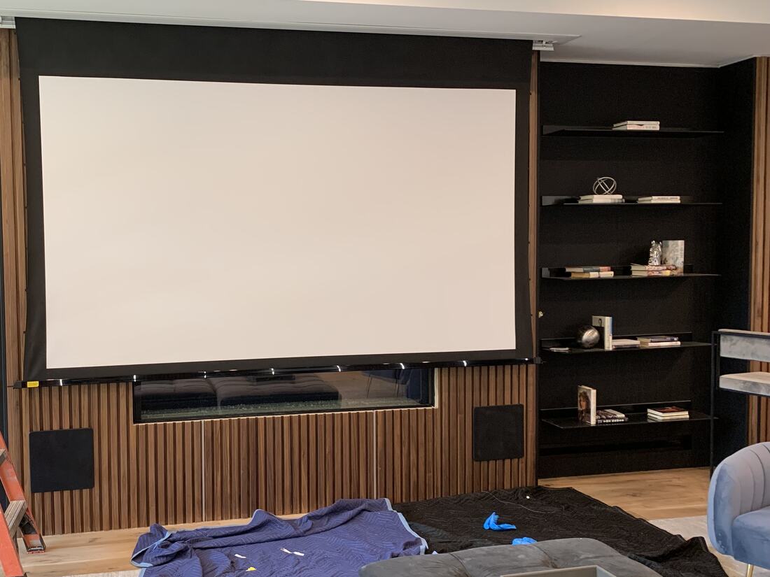 Custom media wall with a large projection screen, slatted wood panel and built-in shelves